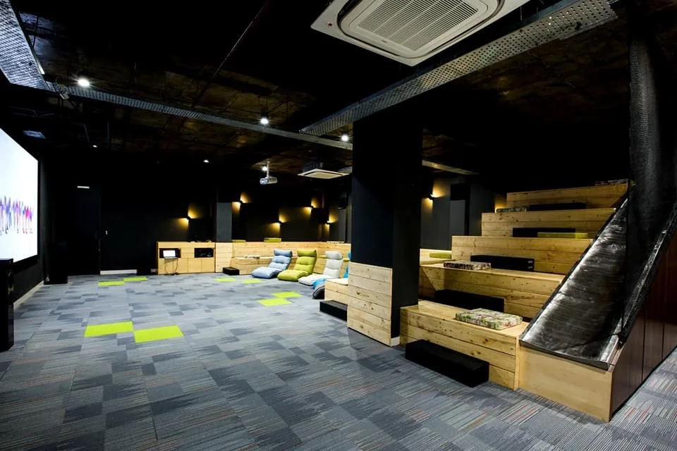Town hall with stepped timber seating, floor cushions, a projection wall and a slide running down beside the steps